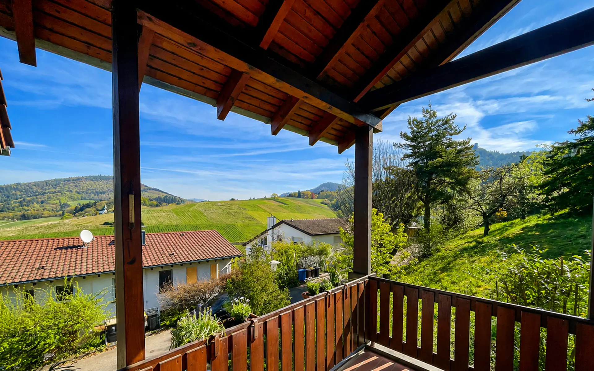 Blick vom überdachten Holzbalkon über Dächer, Weinberge und die Höhen des Schwarzwalds