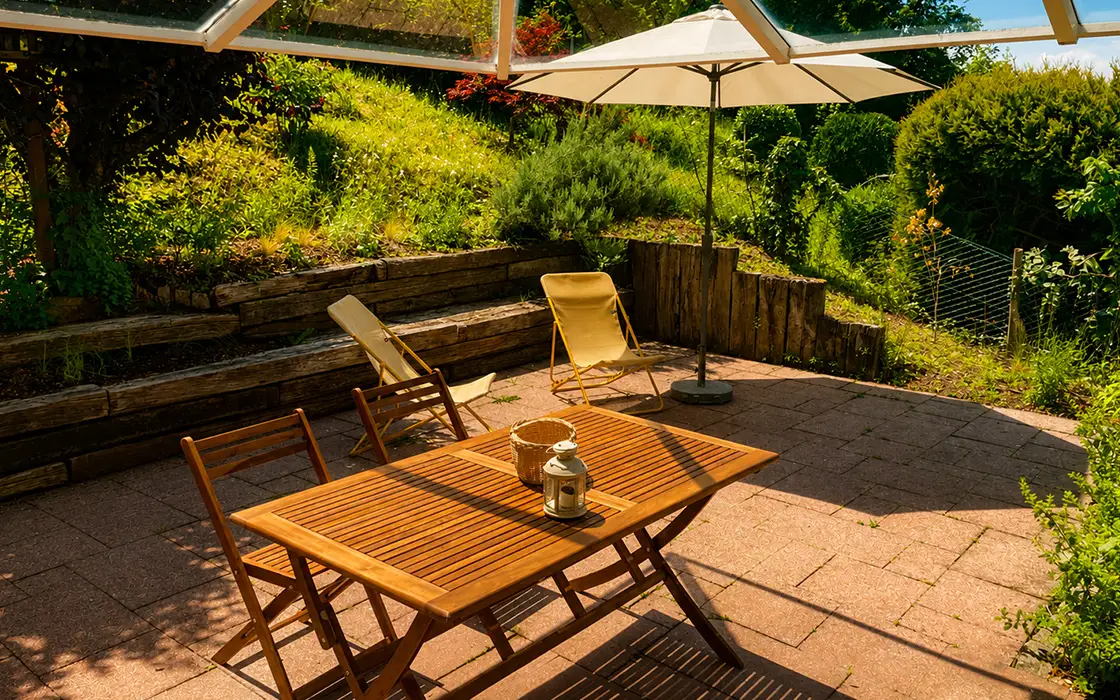 Terrasse mit Holztisch, Liegestühlen und Sonnenschirm im Hang-Garten
